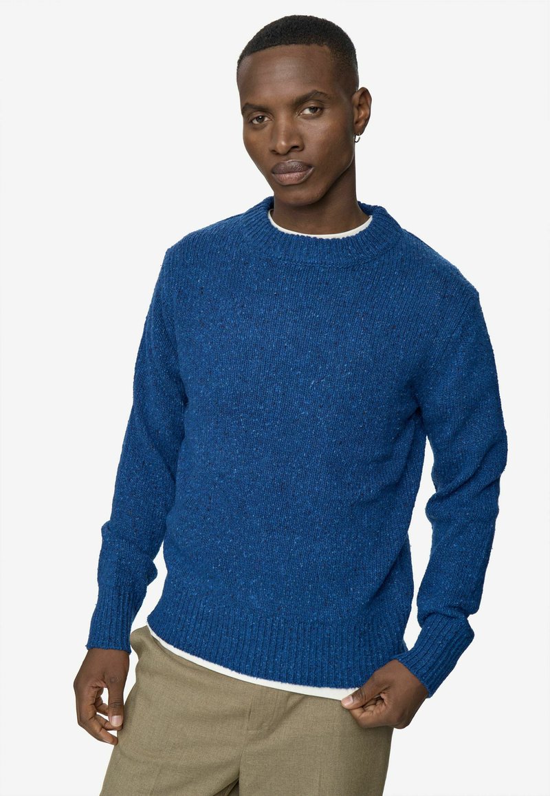 Tengerészkék kötött pulóver kerek nyakkivágással, bordázott mandzsettákkal és alsó szegéllyel. A szöveten texturált minta és finom pici foltok találhatóak.