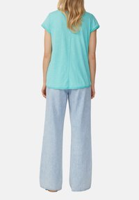 Haut turquoise à manches courtes avec un col rond, associé à un pantalon en denim bleu clair à jambes larges. Texture lisse, coupe décontractée.