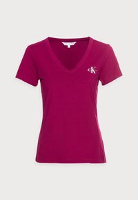 Magenta T-Shirt aus Baumwolle mit V-Ausschnitt und kurzen Ärmeln, mit einem kleinen weißen Logo auf der linken Seite der Brust.