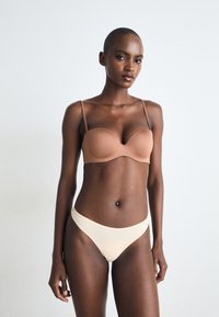 Soutien-gorge rembourré marron avec fines bretelles, associé à un slip de bikini beige clair. Tissu lisse, design sans couture, style minimaliste.