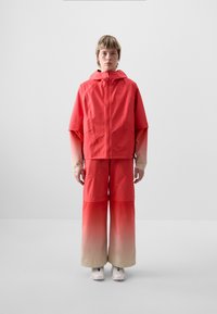 Red waterproof jacket with adjustable hood, paired with red gradient pants fading to beige. Smooth texture, loose fit, with visible seams.