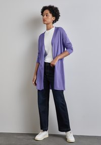 Lavendel öppen förfront cardigan med långa ärmar, lager på en vit t-shirt, ihop med mörka jeans och vita sneakers.