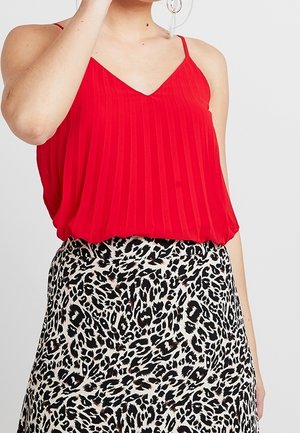 Kobieta ubrana w czerwony, bezrękawnik plisowany top w połączeniu z czarno-białą spódnicą w cętki lamparta.