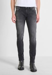 Jeans de mezclilla negra con corte ajustado, que presentan un acabado desgastado, cinco bolsillos y costuras en contraste. Combinados con botas negras a los tobillos.