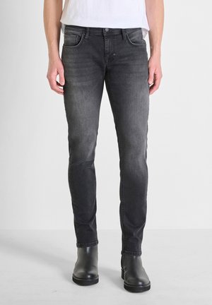 Jeans de mezclilla negra con corte ajustado, que presentan un acabado desgastado, cinco bolsillos y costuras en contraste. Combinados con botas negras a los tobillos.
