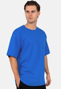 T-shirt en coton bleu avec un col rond, des manches courtes et une coupe décontractée. Coutures renforcées et texture lisse. Sans motifs ni accents.