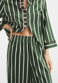 Conjunto de pijama a rayas verdes con rayas verticales blancas, ribete rojo de acento y un ajuste holgado con cintura elástica en los pantalones.