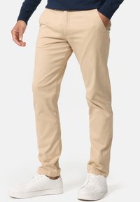 Beige chinos lavet af en bomuldsblanding, med lige ben-design og sidelommer, parret med hvide sneakers. Glat tekstur, skræddersyet pasform.