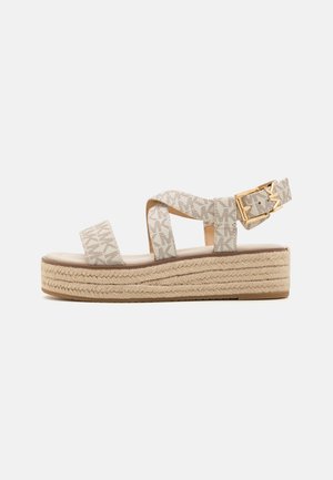 Sandale à plateforme beige avec semelle en corde tissée, deux brides en tissu sur le pied, bride à la cheville avec boucle dorée et motif monogramme subtil.