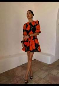 Vestido floral preto com flores laranja brilhantes, mangas bufantes e saia rodada. Os sapatos apresentam um design estampado com bico arredondado.