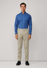 Lichtblauw overhemd met knoopsluiting in een slim fit, gecombineerd met beige broek en marineblauwe schoenen. Knopdetails op het overhemd, platte voorkant van de broek.