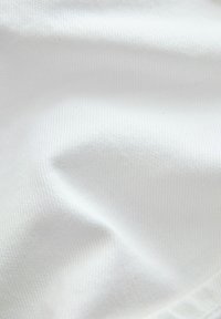 Tissu blanc aux plis doux et à la texture finement tissée, présentant de légers plis et une surface lisse sous un éclairage diffus.