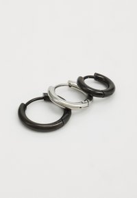Three hoop earrings arranged horizontally: one shiny silver, one matte black, and one glossy black, all with smooth curves and a seamless design.