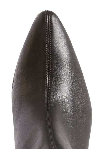 Zapato de cuero negro con punta afilada, de textura suave y costura visible a lo largo de la costura. La parte superior presenta un diseño elegante y minimalista.