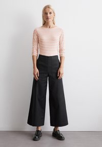 Striped pink long-sleeve top paired with high-waisted black wide-leg pants. Model wears black loafers, fabric appears smooth.