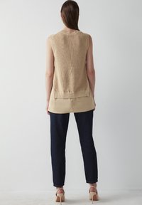 Beige stickad ärmlös topp med ribbad nederkant, över en krämfärgad tunika, matchad med mörkblå smala jeans och beige klackar.