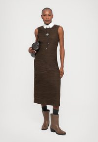 Rochie midi bohemă, texturată, de culoare maro, cu o formă ajustată, guler alb și pliseuri orizontale complicate. Asortată cu șosete gri și cizme până la gleznă bej.