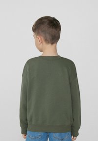 Tmavě zelená mikina na pulovr s žebrovanými manžetami a spodním lemem, měkká textura, volný střih a kulatý výstřih, nošena dítětem z pohledu zezadu.