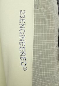 Leichtes, cremefarbenes Gewebe mit strukturierter Oberfläche und Rastermuster. Auf der Seite prangt die auffällige silberne Aufschrift "23ENGINEERED".