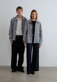 Γκρι πουκάμισα με διακριτικό μοτίβο, σε συνδυασμό με σκούρα τζιν φαρδιάς γραμμής. Απλός σχεδιασμός, άνετη εφαρμογή και ανθεκτικό ύφασμα. Τα υποδήματα είναι μαύρα.