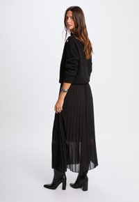 Sort strikket sweater og plisseret sort nederdel med sølvprikkede detaljer, parret med sorte ankelstøvler, der viser en slank, lagdelt silhuet.