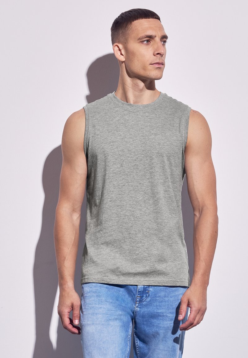 Graues ärmelloses T-Shirt aus weichem Stoff mit rundem Ausschnitt. Kombiniert mit hellblauen Jeans. Schlichtes Design, ohne Muster.