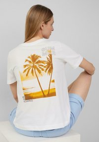 T-shirt blanc à manches courtes avec un motif de palmier jaune au dos et le texte "ÉTÉ" ainsi que "DÉTENDU, RAFRAÎCHI, RECHARGÉ."