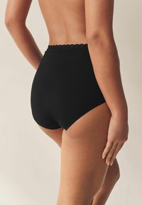 Melnas augsta vidukļa biksītes ar mežģīņu apdari, ar gludu tekstūru un minimālistisku dizainu. Aizmugures skats izceļ griezumu un pieguli.