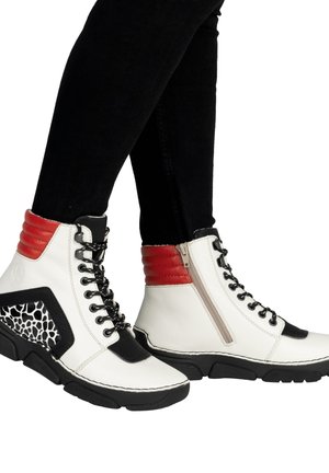 Białe botki do kostki z czarnymi podeszwami, czerwonymi wyściełanymi kołnierzami, czarnymi sznurowadłami, bocznymi zamkami błyskawicznymi oraz czarno-białymi panelami w wzory, noszone z czarnymi spodniami.