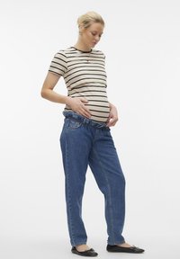 Randig beige och svart kortärmad topp i kombination med lösa blå jeans med elastiskt midjeband, bärs av en kvinna med en synlig graviditetsslutt.