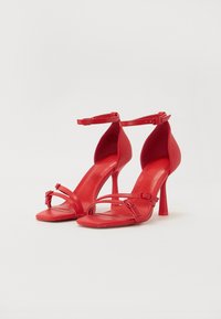 Sandales à talons hauts en cuir rouge avec bride de cheville, présentant deux fines brides sur le devant du pied et un design à bout pointu.