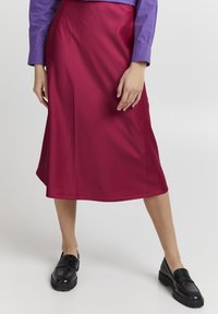Magenta satiinimidi-seelik, millel on sile tekstuur, peene lähega ja A-jooneline siluett, koos mustade loafers'itega.
