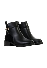 Bottines noires en cuir lisse, avec un léger talon et une fermeture éclair latérale. Elles possèdent une bride décorative avec une boucle dorée.