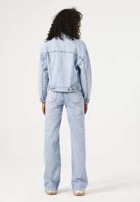 Chaqueta y pantalones de mezclilla azul claro, con un ajuste relajado, textura desgastada y detalles de costura clásicos. La vista trasera muestra un diseño entallado.