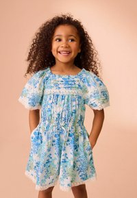 Blommig klänning i ljusblått med puffärmar, spetsdetaljer, elastisk midja och sidofickor. Invecklade mönster i blått och grönt.