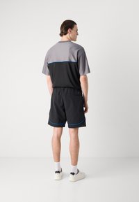 Camiseta deportiva de manga corta, bicolor en gris y negro con detalles en azul, combinada con pantalones cortos negros con acentos azules y una cintura elástica.