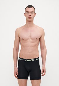 Črne Nike boksarske hlače z širokim elastikastim pasom, ki ima svetlo zeleni logotip, oprijet kroj in gladko teksturo tkanine.