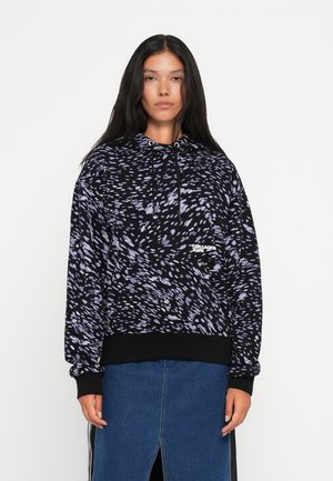 Felpa nera con motivo astratto viola, coulisse e tasca frontale. Polsini e orlo a costine. Abbinata a una gonna di denim.