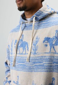 Katoenen hoodie met een beige en blauw ontwerp met cowboys en cactussen, trekkoord in de kap en een zachte textuur.
