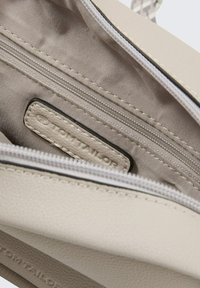 Beige synthetische Handtasche mit einer glatten Textur im Inneren, ausgestattet mit einer Reißverschlusstasche und einem gestickten Etikett mit dem "TOM TAILOR"-Logo.