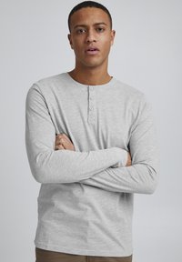 Lys grå langermet henley-skjorte med rund hals, tre-knappers front lukking og myk tekstur, kombinert med khaki bukser.
