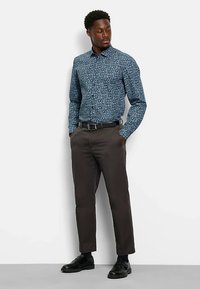 Langärmliges Hemd mit Knöpfen in Dunkelblau mit floralen Muster, kombiniert mit dunkler Hose und schwarzen Schuhen. Glatter Stoff und maßgeschneiderte Passform.