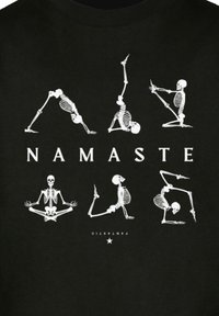 Schwarzes T-Shirt mit weißen Skelettillustrationen in verschiedenen Yoga-Posen. Der Text lautet "NAMASTE" in fetter, zentraler Schrift.