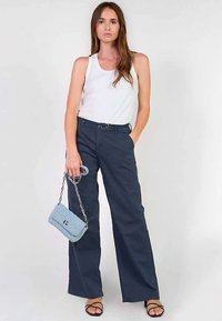 Wijde marineblauwe broek van katoenmix, gecombineerd met een wit tanktopje. Geaccentueerd met een lichtblauwe handtas en zwarte sandalen met bandjes.