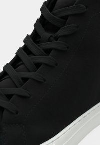 Svarte lær sneakers med jevn tekstur, flate svarte snører og en hvit gummisåle med et minimalistisk design og diskret søm.