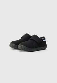 Scarpe nere slip-on realizzate in tessuto morbido con suola testurizzata, dotate di una larga cinghia in Velcro per una facile calzata e un design minimale.