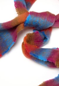 Bufanda multicolor hecha de un material suave y peludo que presenta tonos de azul, rosa, marrón y naranja, con bordes deshilachados y una forma retorcida.