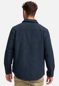Camisa azul marino de tejido, con botones y cuello, que presenta mangas largas y un dobladillo recto. El material parece suave y texturizado.