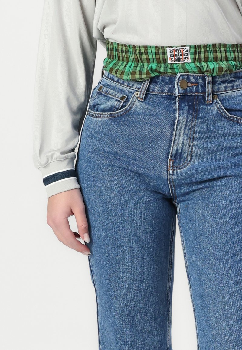 Top de manga larga gris con el logo de Nike, combinado con jeans de mezclilla azul de talle alto y una cinturilla elástica a cuadros verdes.
