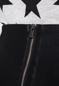Prenda de cuero negra con una cremallera plateada visible. La textura es suave con un ligero brillo, complementada por una tela gris que presenta un patrón de estrellas en la parte superior.